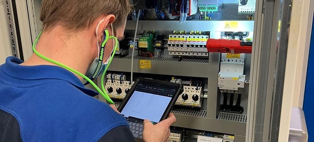 Technician checking industrial electrical components with a tablet during an equipment inventory.